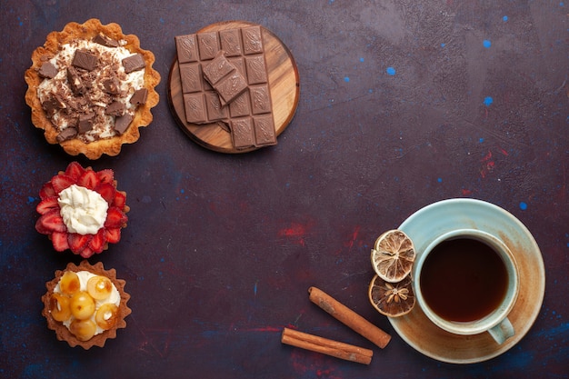 Vista superior de deliciosos pasteles con crema de chocolate y frutas con té en la superficie oscura