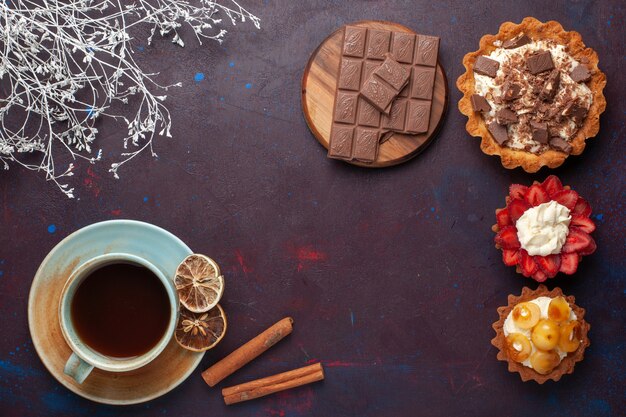 Vista superior de deliciosos pasteles con crema de chocolate y frutas con té en la superficie oscura