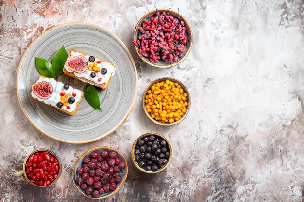 Vista superior de deliciosos pasteles de crema con diferentes frutas sobre fondo claro