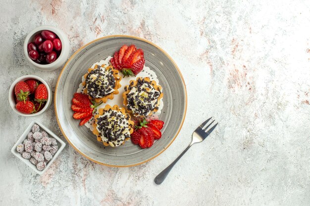 Vista superior de deliciosos pasteles con crema y fresas en la superficie blanca celebración de cumpleaños pastel de galletas dulces