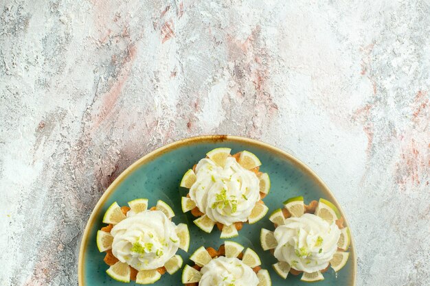 Vista superior de deliciosos pasteles con crema y rodajas de limón en la superficie blanca pastel galletas galletas té dulce azúcar