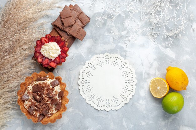Vista superior deliciosos pasteles cremosos con barras de chocolate y limón en el escritorio blanco pastel galleta dulce azúcar hornear
