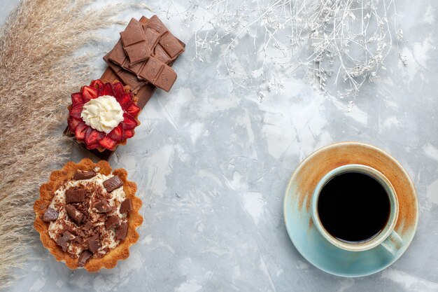 Vista superior deliciosos pasteles cremosos con barras de chocolate y té en el escritorio blanco pastel galleta hornear azúcar dulce