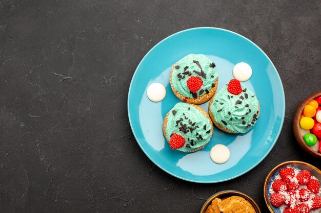 Vista superior de deliciosos pasteles cremosos con caramelos en el color oscuro de las galletas del caramelo de la galleta del postre de la torta del escritorio