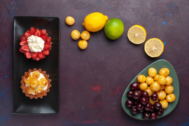 Vista superior de deliciosos pasteles cremosos dentro de la placa con limones frescos y frutas sobre una superficie oscura