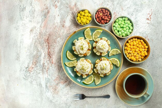 Vista superior deliciosos pasteles cremosos con rodajas de limón en el escritorio blanco pastel galleta galleta crema té dulce