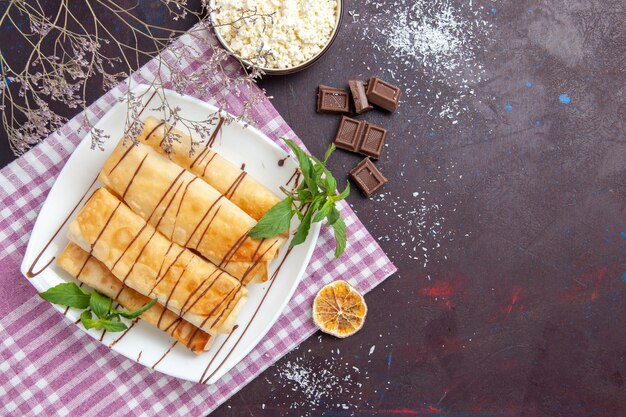 Vista superior de deliciosos pasteles dulces con barras de chocolate en el espacio oscuro