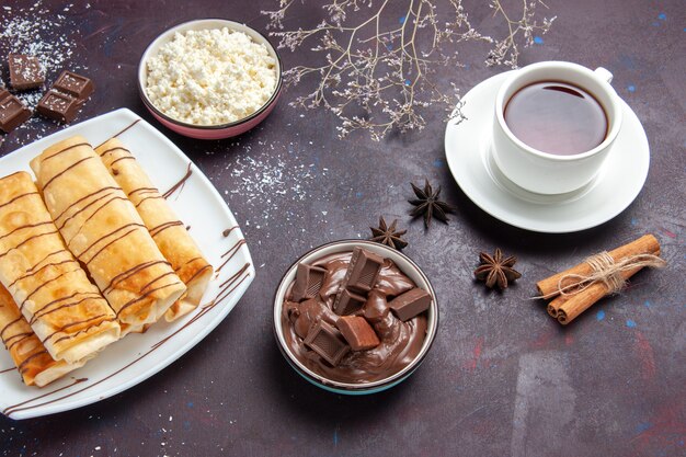 Vista superior deliciosos pasteles dulces con chocolate y taza de té en el espacio oscuro