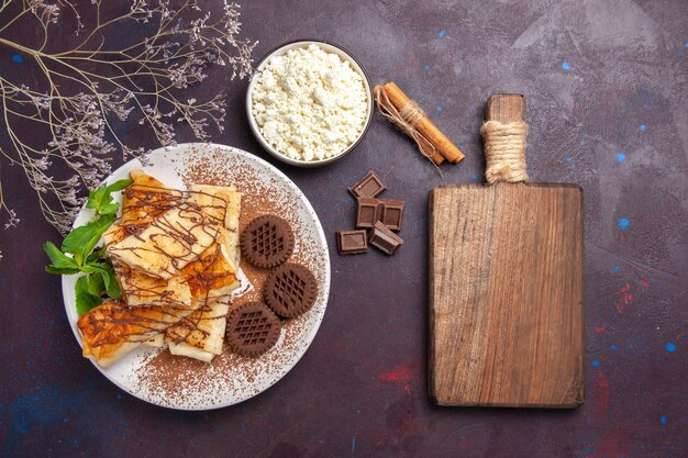 Vista superior de deliciosos pasteles dulces con galletas de chocolate en el escritorio oscuro