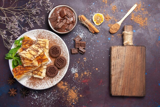 Vista superior de deliciosos pasteles dulces con galletas de chocolate en el espacio oscuro