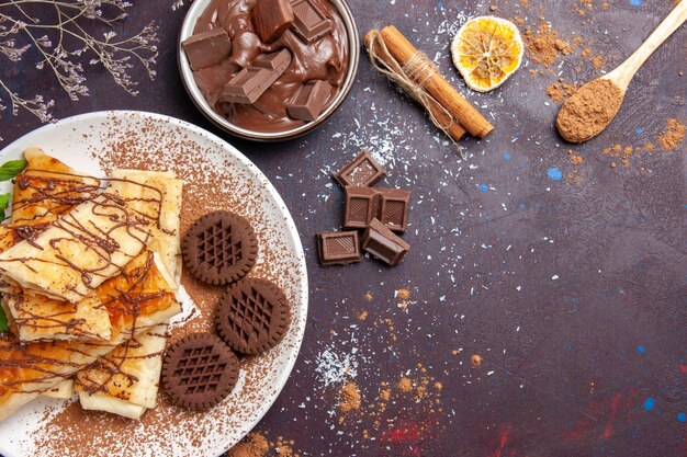 Vista superior de deliciosos pasteles dulces con galletas de chocolate en el espacio oscuro