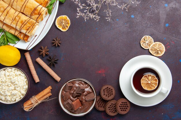 Vista superior de deliciosos pasteles dulces con galletas y té en el espacio oscuro