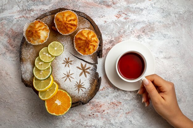 Vista superior de deliciosos pasteles dulces con rodajas de limón y una taza de té en el escritorio blanco