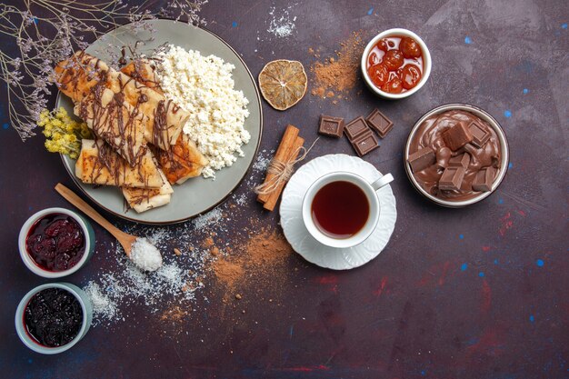 Vista superior deliciosos pasteles dulces en rodajas con una taza de té y requesón sobre fondo oscuro galleta galleta azúcar pastel dulce pastelería