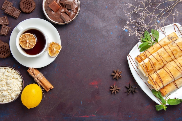 Vista superior de deliciosos pasteles dulces con taza de té, chocolate y galletas en el espacio oscuro