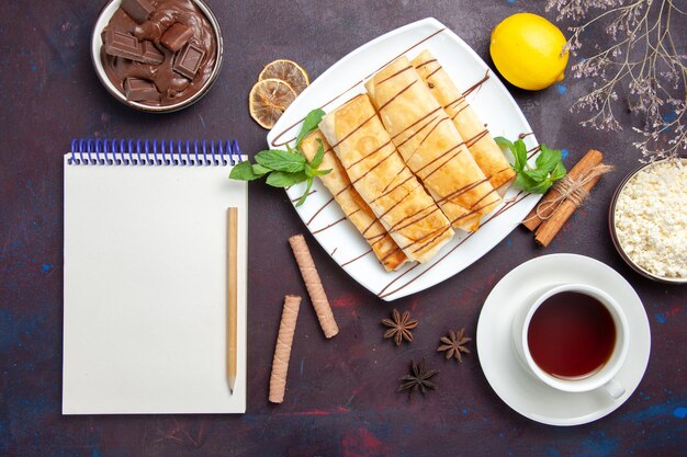 Vista superior deliciosos pasteles dulces con taza de té en el espacio oscuro