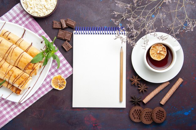 Vista superior de deliciosos pasteles dulces con taza de té y galletas en el espacio oscuro