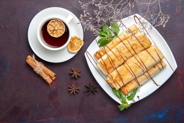 Vista superior deliciosos pasteles dulces con té en el espacio oscuro