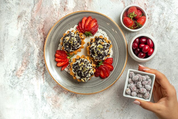 Vista superior de deliciosos pasteles con fresas y dulces en la superficie blanca celebración de cumpleaños pastel de galletas dulces