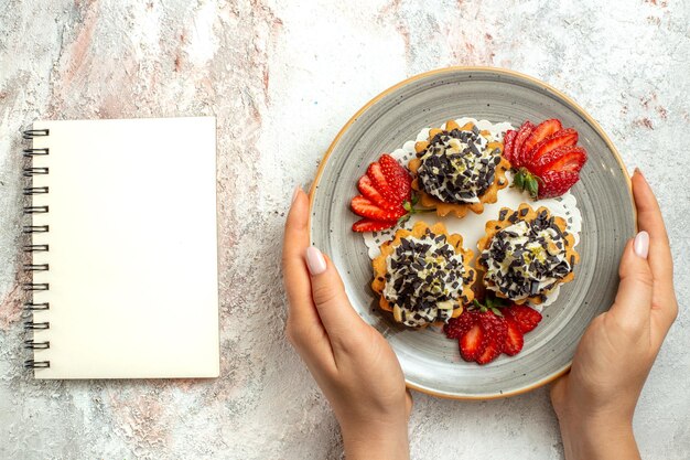 Vista superior de deliciosos pasteles con fresas en el escritorio blanco celebración de cumpleaños pastel de galletas dulces