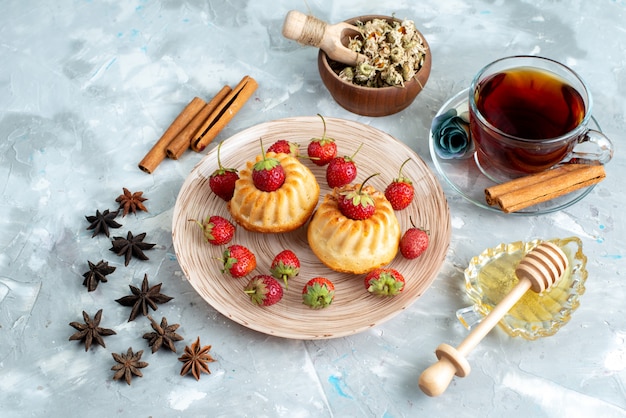 Una vista superior de deliciosos pasteles con fresas rojas, canela y galleta de pastel de té