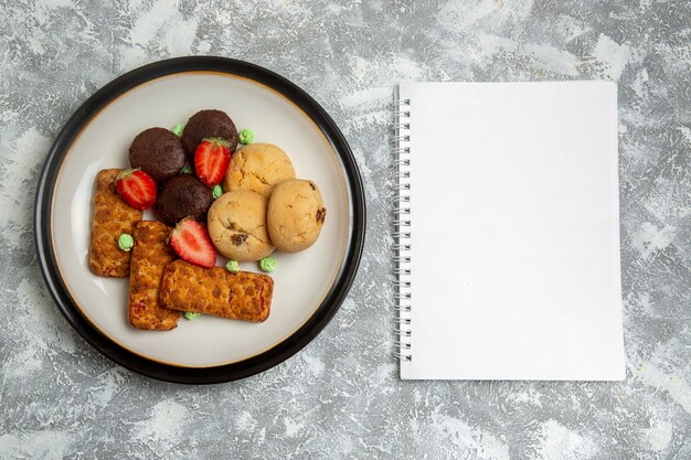 Vista superior de deliciosos pasteles con galletas y fresas en el fondo blanco claro galleta pastel de azúcar tarta dulce galleta de té