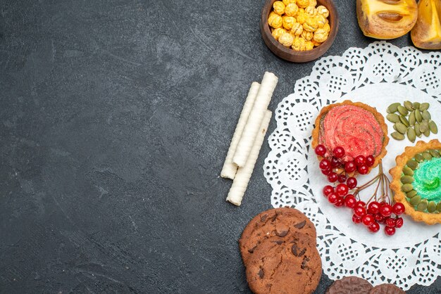 Vista superior de deliciosos pasteles con galletas y frutas en el dulce pastel de postre de mesa oscura