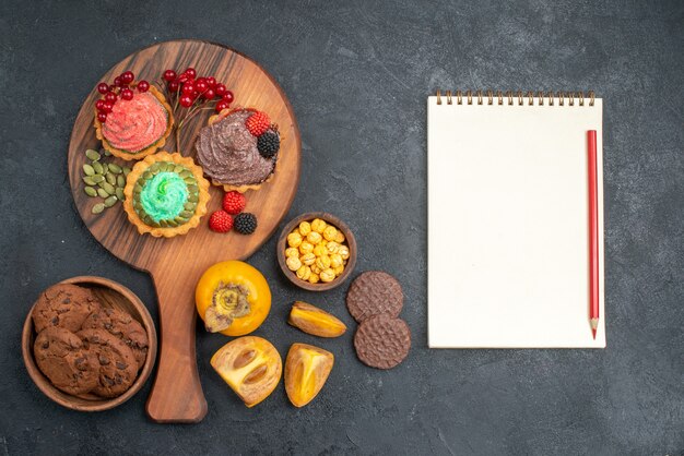 Vista superior de deliciosos pasteles con galletas y frutas en el pastel de pastel dulce de mesa oscura