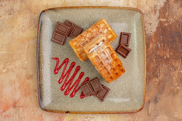 Vista superior deliciosos pasteles de gofres con barras de chocolate en el fondo marrón