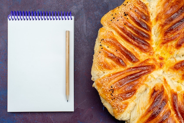 Vista superior de deliciosos pasteles horneados bollo formado pastelería con bloc de notas sobre el fondo oscuro.