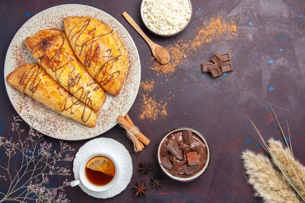 Vista superior de deliciosos pasteles horneados con requesón y té en el espacio oscuro