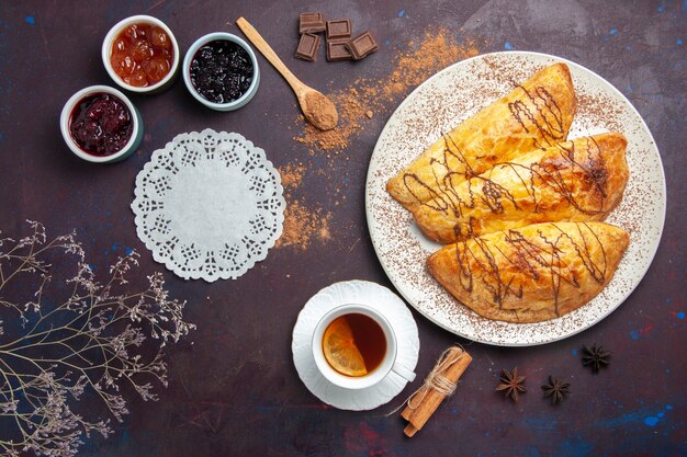 Vista superior de deliciosos pasteles horneados con taza de mermelada de té en el espacio oscuro