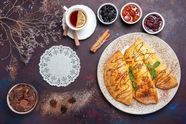 Vista superior de deliciosos pasteles horneados con taza de mermelada de té en el espacio oscuro