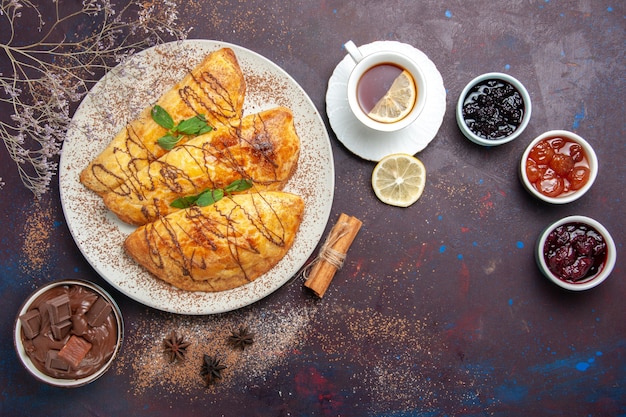 Vista superior de deliciosos pasteles horneados con taza de mermelada de té en el espacio oscuro