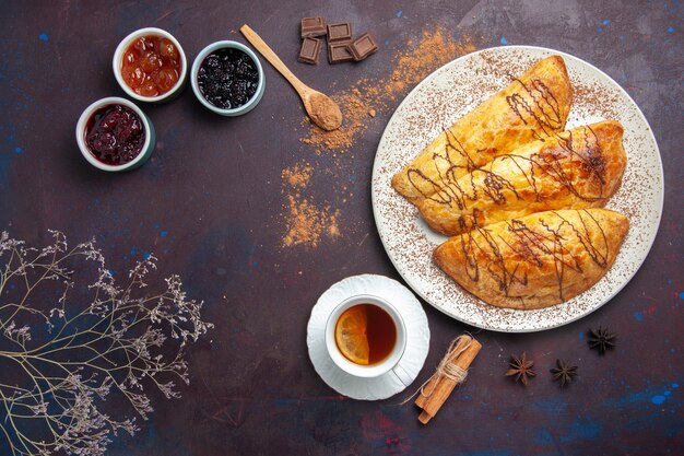 Vista superior de deliciosos pasteles horneados con taza de mermelada de té en el espacio oscuro