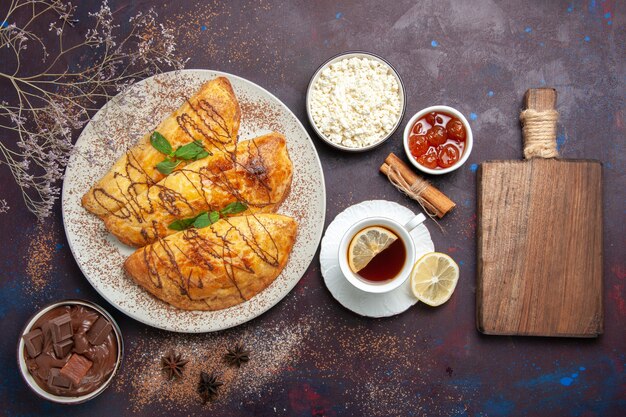 Vista superior de deliciosos pasteles horneados con taza de té en el escritorio oscuro