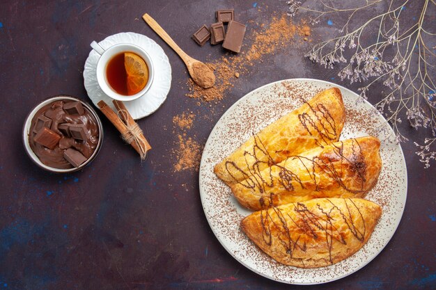 Vista superior de deliciosos pasteles horneados con taza de té en el espacio oscuro