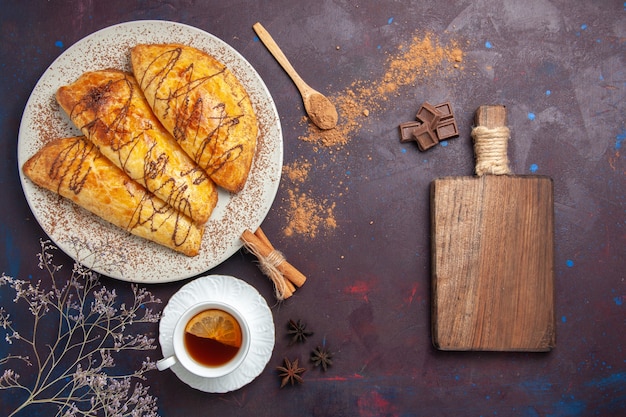 Vista superior de deliciosos pasteles horneados con taza de té en el espacio oscuro