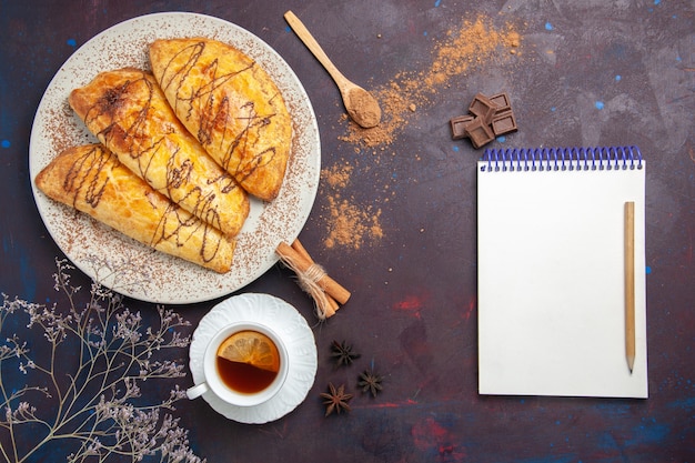 Vista superior de deliciosos pasteles horneados con taza de té en el espacio oscuro