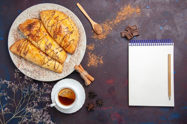 Vista superior de deliciosos pasteles horneados con taza de té en el espacio oscuro