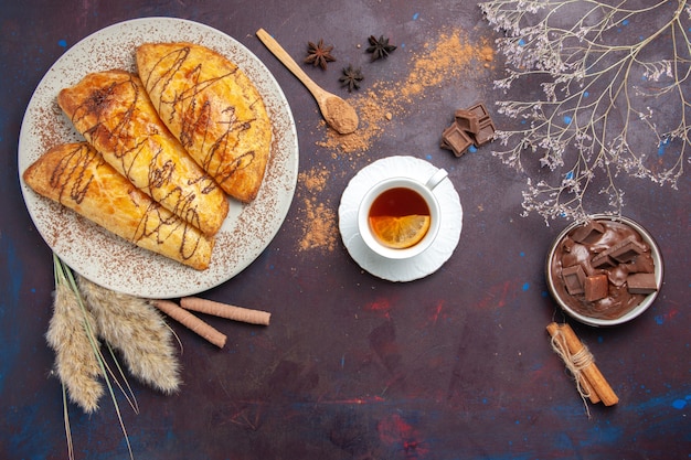 Vista superior de deliciosos pasteles horneados con taza de té en el espacio oscuro