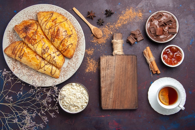 Vista superior de deliciosos pasteles horneados con taza de té y requesón en el espacio oscuro