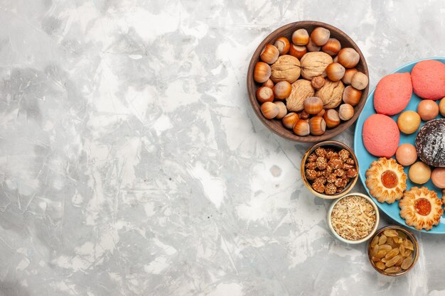 Vista superior de deliciosos pasteles con nueces macarons y galletas en el escritorio blanco