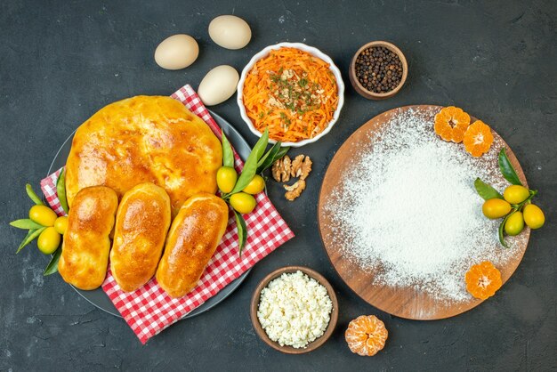 Vista superior de deliciosos pasteles recién horneados y queso pimientos huevos harina mandarinas en la ensalada de tabla de cortar de madera en blackground oscuro