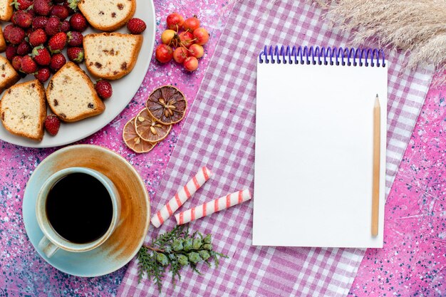 Vista superior de deliciosos pasteles en rodajas con bloc de notas de café y fresas rojas en el escritorio rosa claro