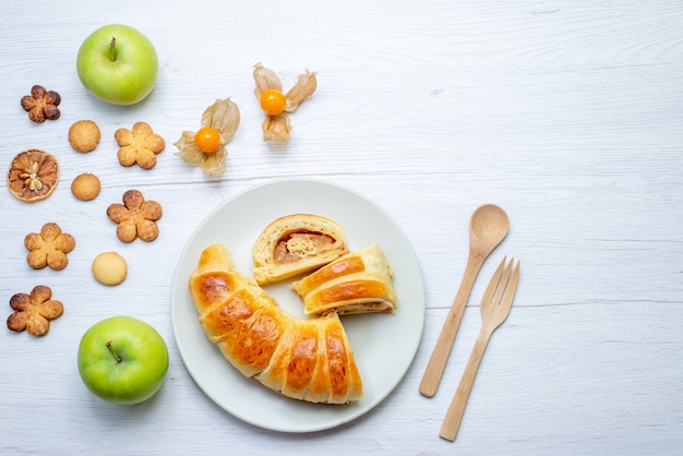 Vista superior de deliciosos pasteles en rodajas dentro de la placa con relleno junto con manzanas y galletas en blanco, pastelería galleta galleta azúcar dulce