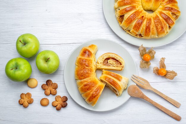 Vista superior de deliciosos pasteles en rodajas dentro de la placa con relleno junto con manzanas verdes y galletas en blanco, galleta de pastelería, azúcar dulce