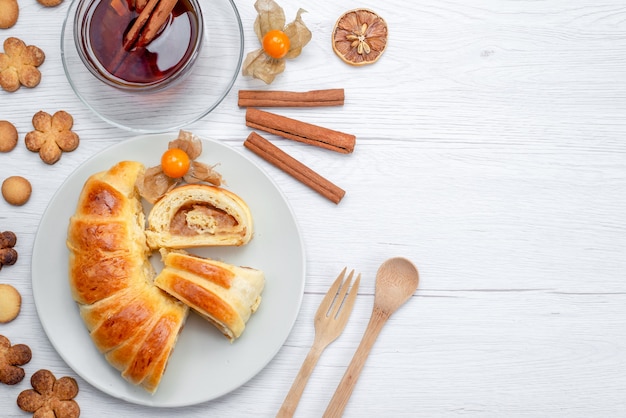 Vista superior de deliciosos pasteles en rodajas dentro de la placa con relleno junto con té canela y galletas en blanco, galleta de pastelería dulce