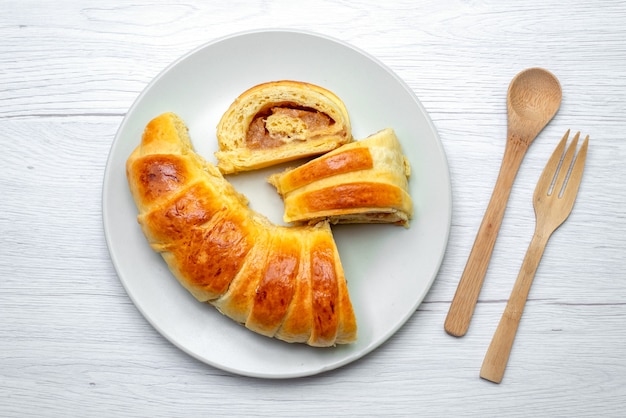 Vista superior de deliciosos pasteles en rodajas dentro del plato con relleno junto con una cuchara de tenedor de madera en el escritorio blanco, pastelería galleta galleta azúcar dulce