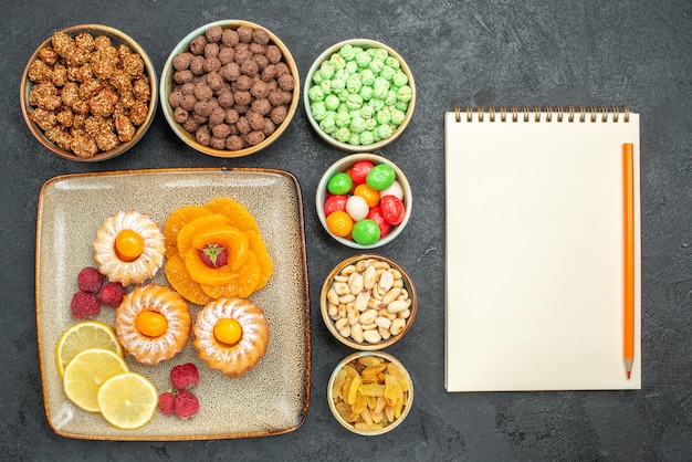 Vista superior de deliciosos pasteles con rodajas de limón, mandarinas y dulces en gris